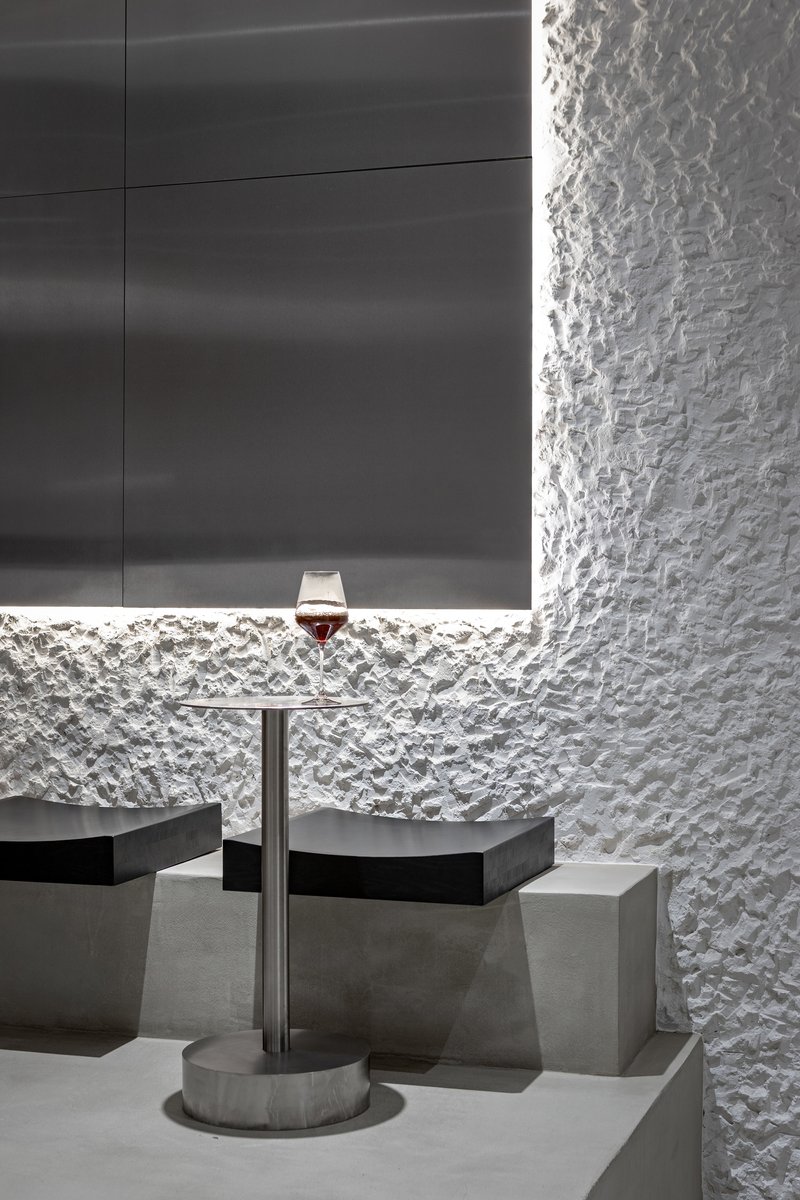 Concrete table with wine glass against textured white wall and backlit horizontal niche