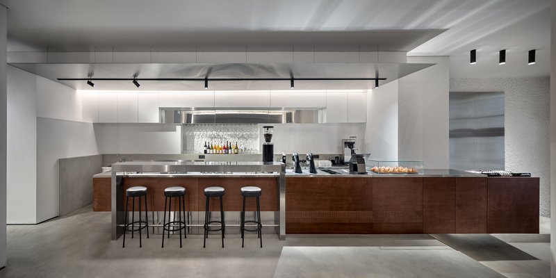 Service counter with walnut base and four bar stools under linear ceiling lighting
