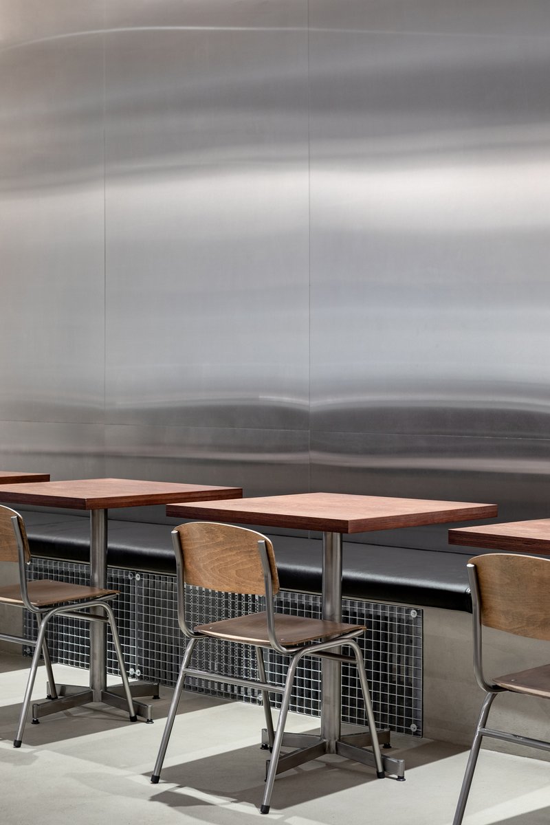 Cafe seating with wood tables and metal chairs against a brushed steel landscape mural
