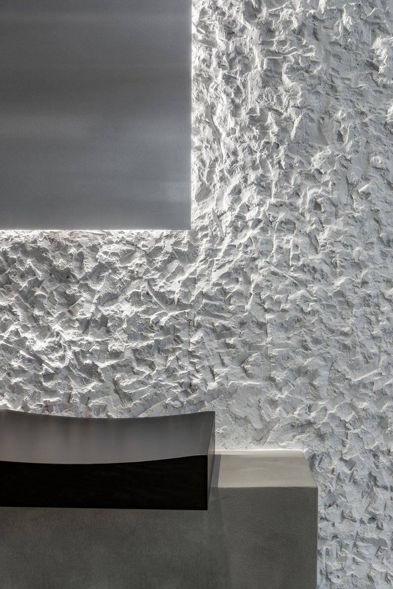 Corner detail where rough white textured plaster meets a recessed dark panel with concealed lighting