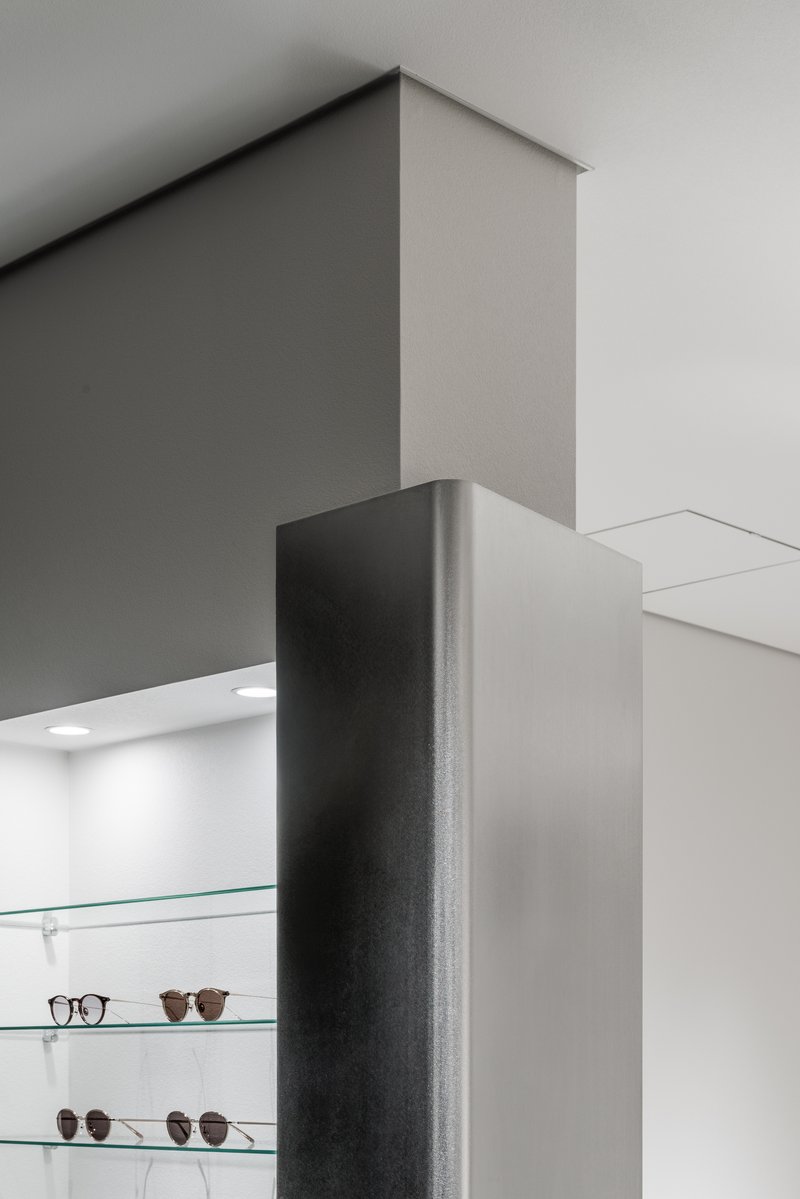 Detail of dark painted column meeting white ceiling near glass shelves displaying eyewear