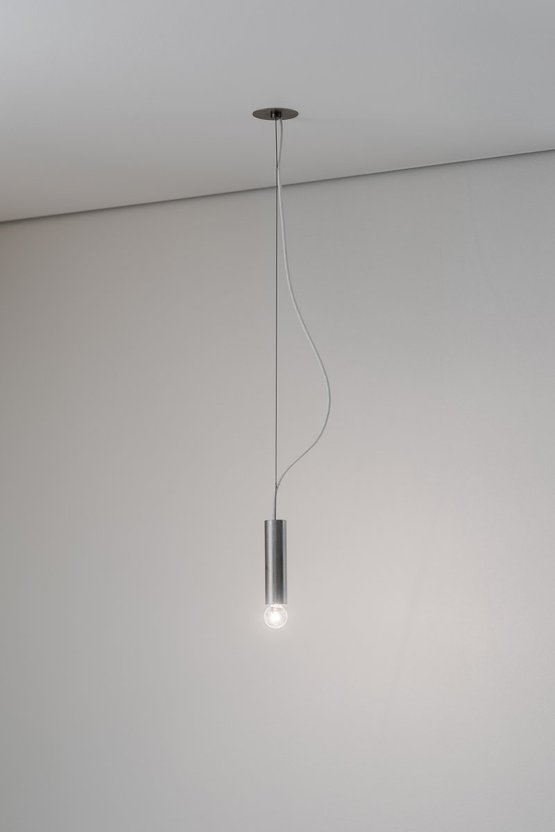 Single pendant light fixture with cylindrical metal shade suspended from ceiling by thin cord
