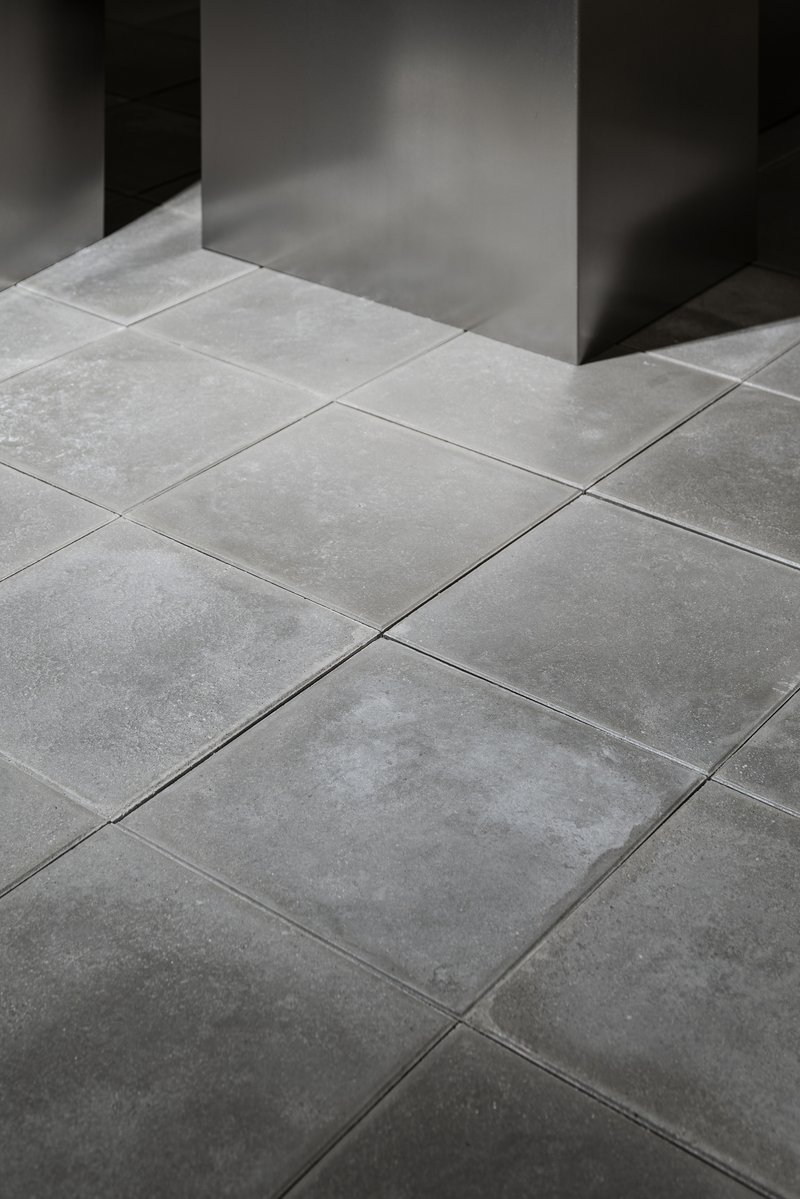 Large format grey stone floor tiles meeting a dark metal column in soft natural light