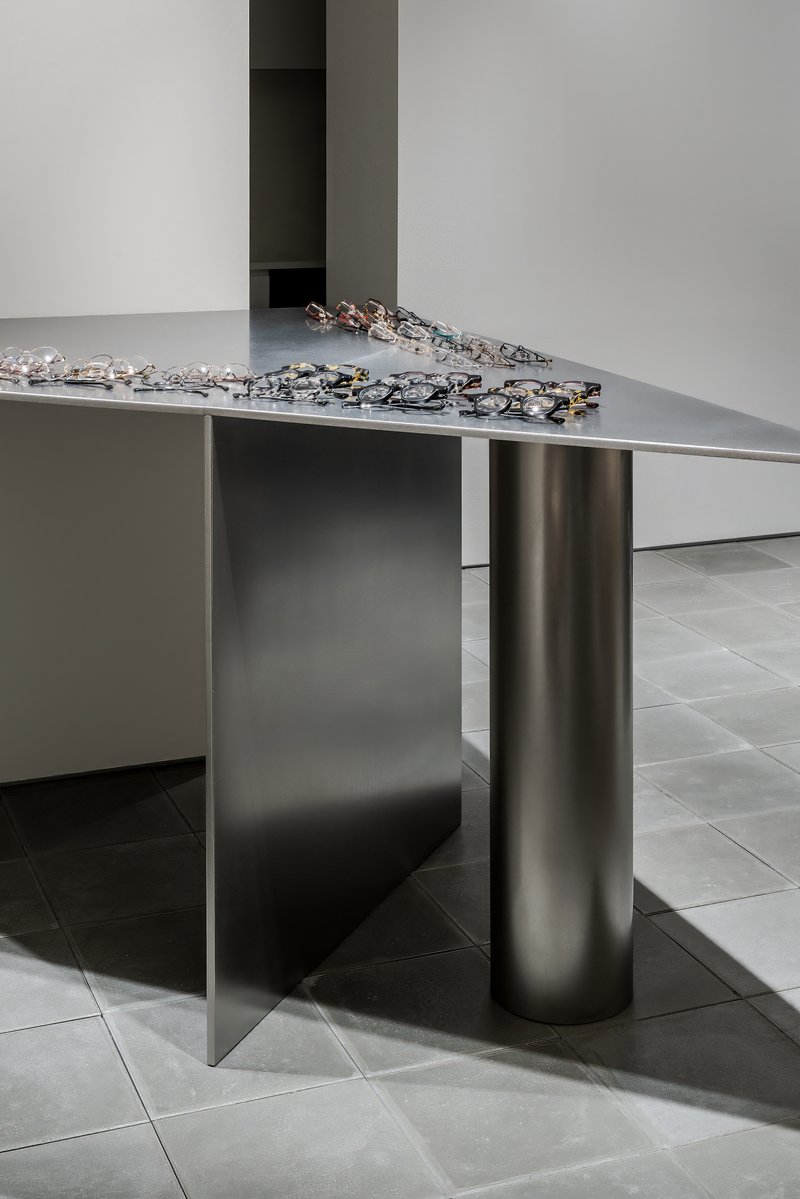 Detail of cylindrical steel column supporting a metal display table with eyeglasses