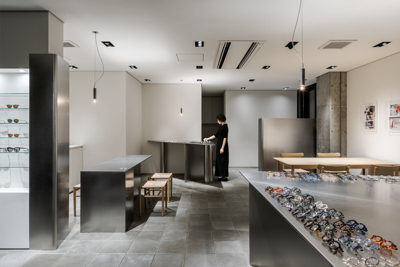Staff member arranging eyeglasses at a display table beneath recessed ceiling fixtures