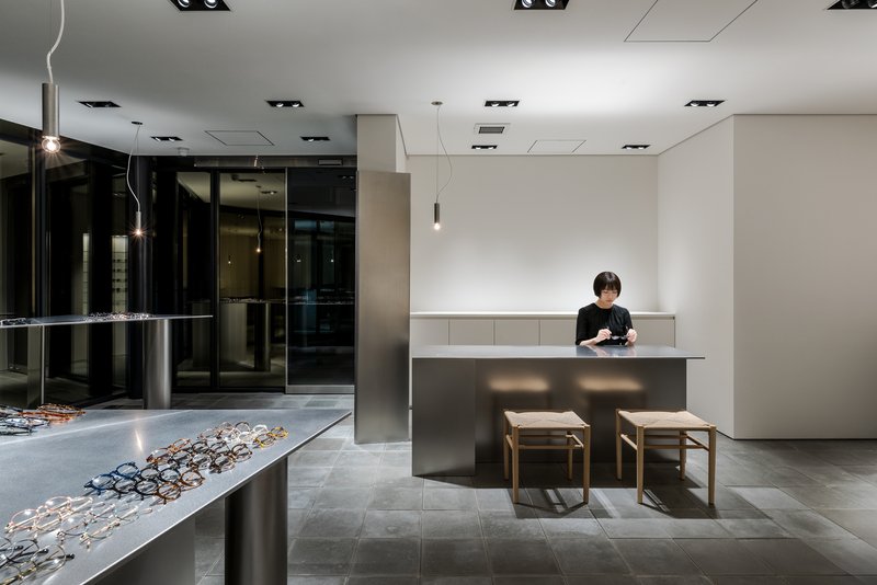 Retail interior with stainless steel display counters lined with eyeglasses and a staff member at the desk