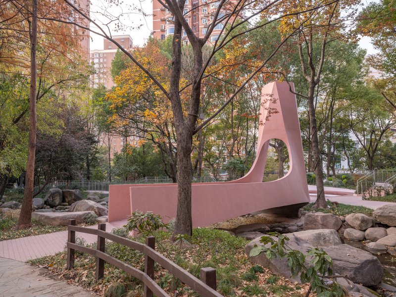 Pink sculptural pavilion spanning boulders and a dry streambed among autumn trees in a park
