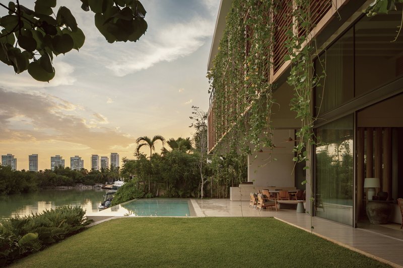 Infinity pool and lawn facing a vertical garden on the rear facade at dusk