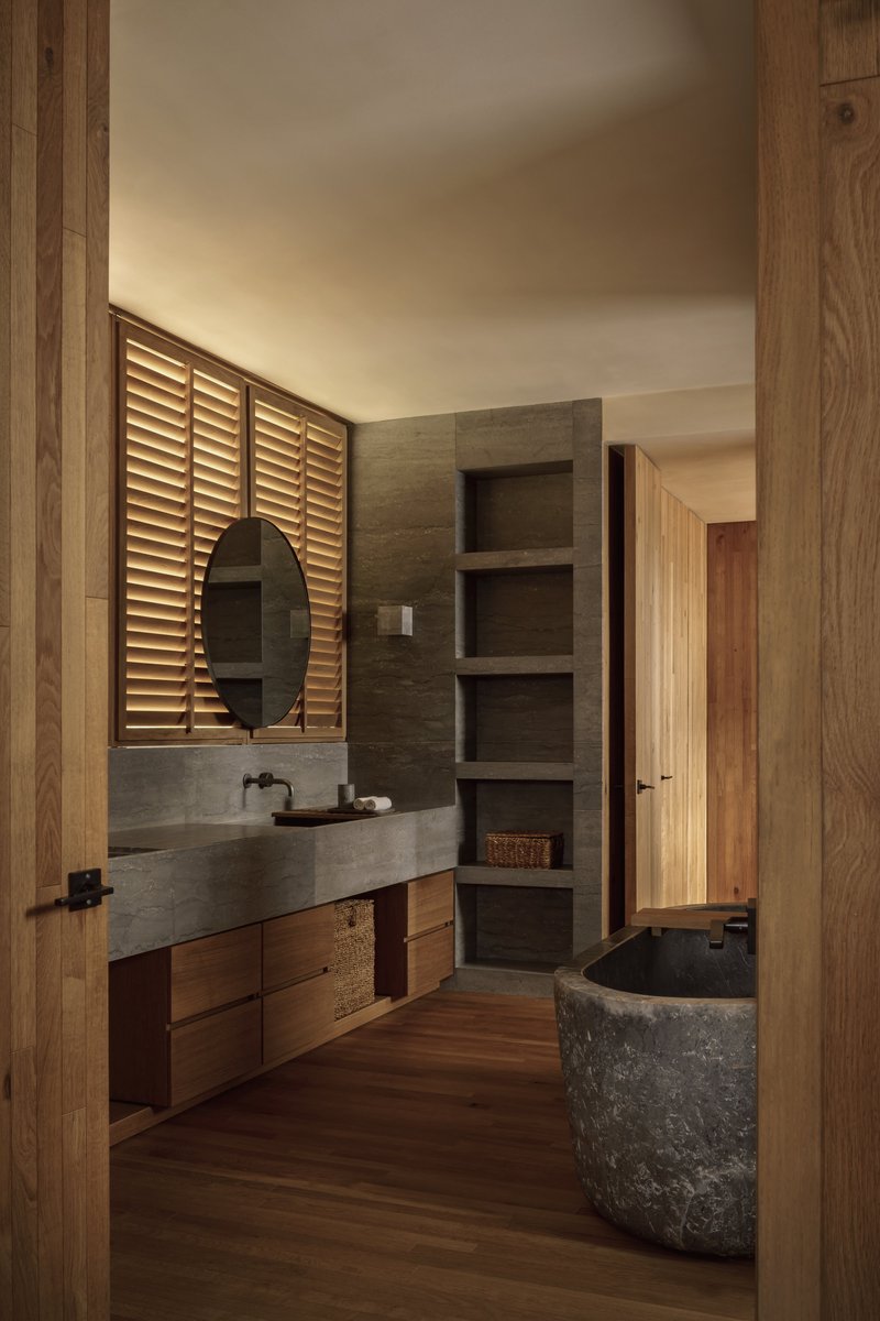 Bathroom with concrete vanity, louvered timber screen, and stone soaking tub beneath wooden flooring