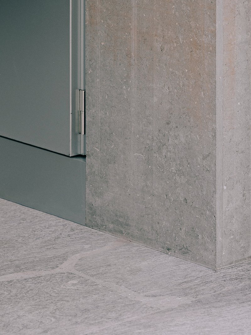 Corner detail where grey metal cabinet meets cast concrete wall and wood flooring