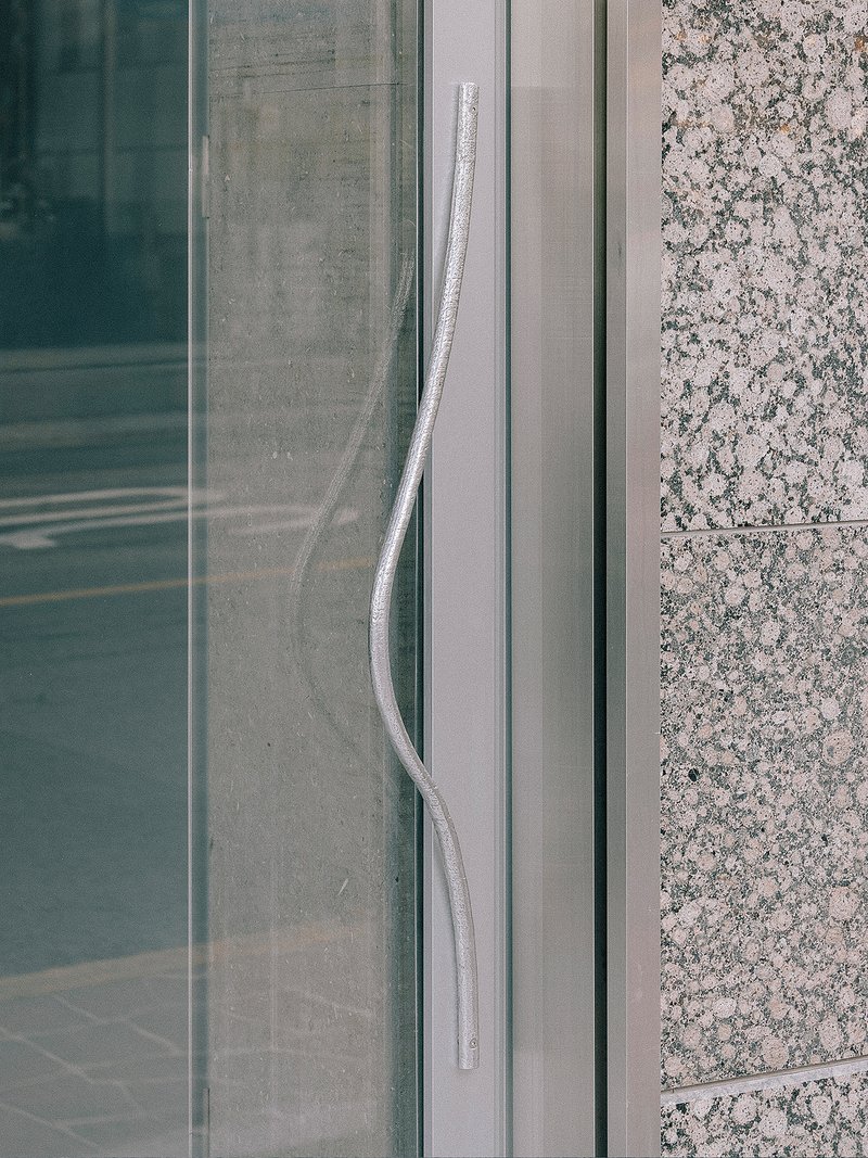 Glass door pull handle set against granite cladding and metal framing system