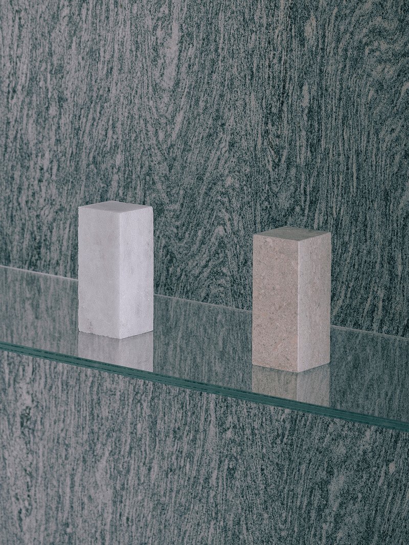 Glass shelf with two stone blocks mounted on textured dark wall panel