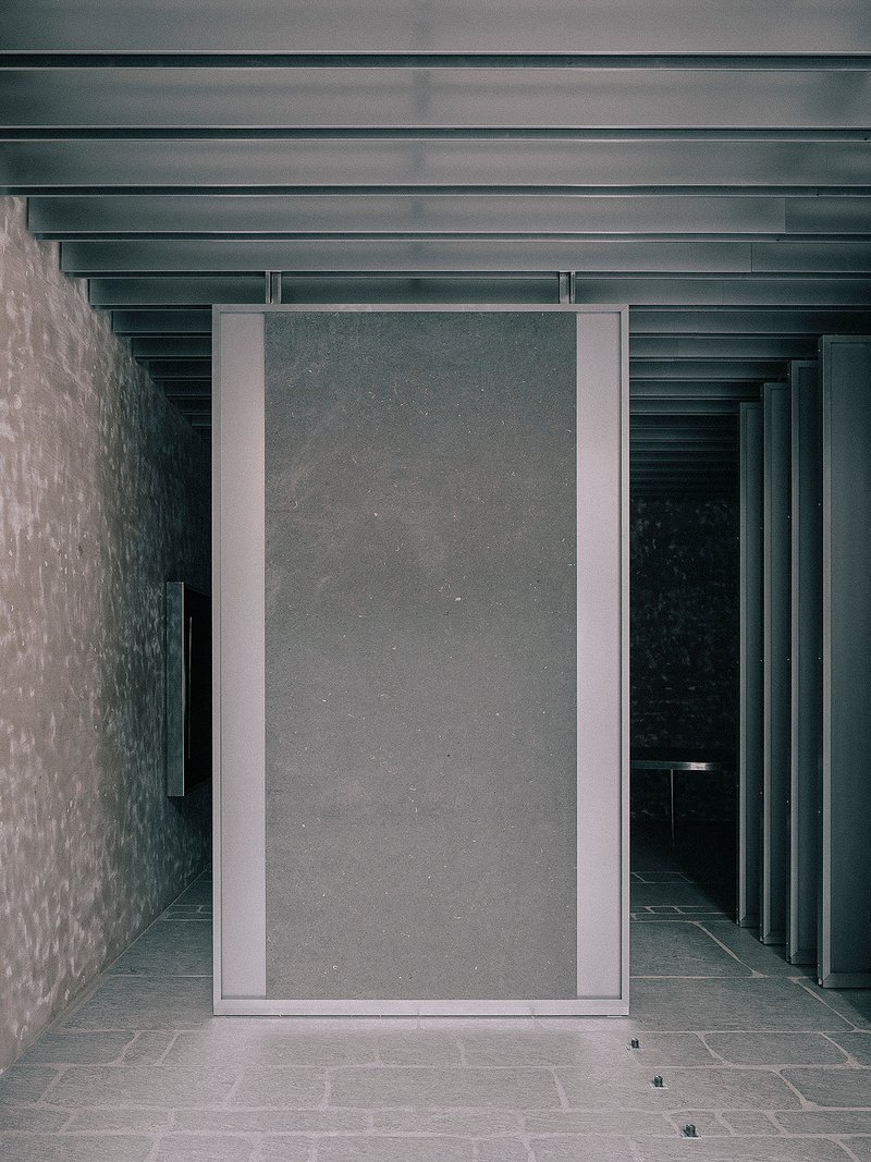 Pivoting metal-framed door panel set between textured concrete walls beneath a ribbed ceiling