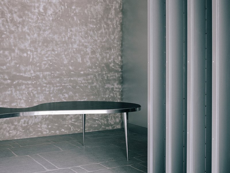 Detail of black curved tabletop with metal legs against textured wall and vertical metal columns
