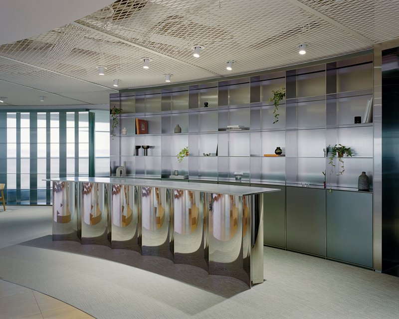Kitchen island with pleated fabric skirt beneath translucent glass shelving wall displaying plants and objects
