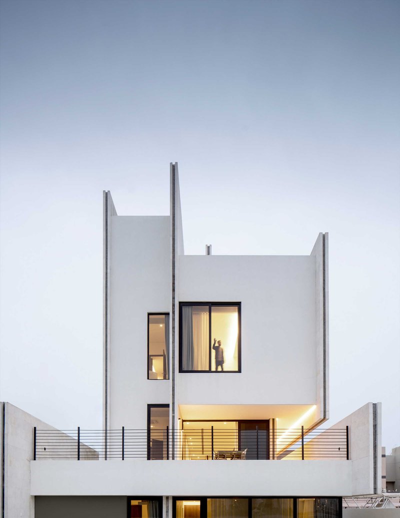Rear facade at twilight showing illuminated windows and terrace with dining furniture behind horizontal wire railings