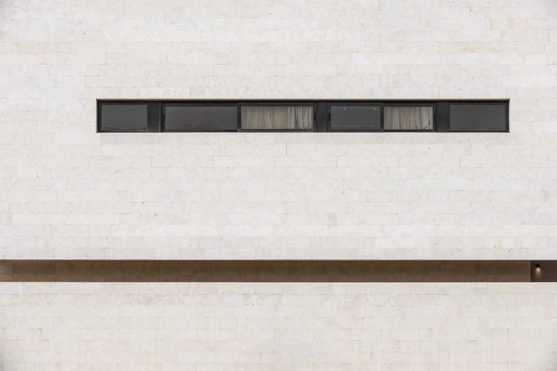 Horizontal ribbon window with six panels set into a pale travertine facade with bronze detailing below