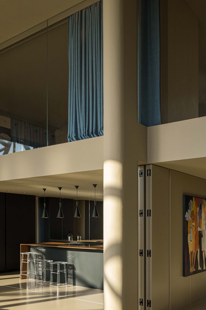 Double-height living space with blue curtains above a mezzanine and kitchen island illuminated by sunlight