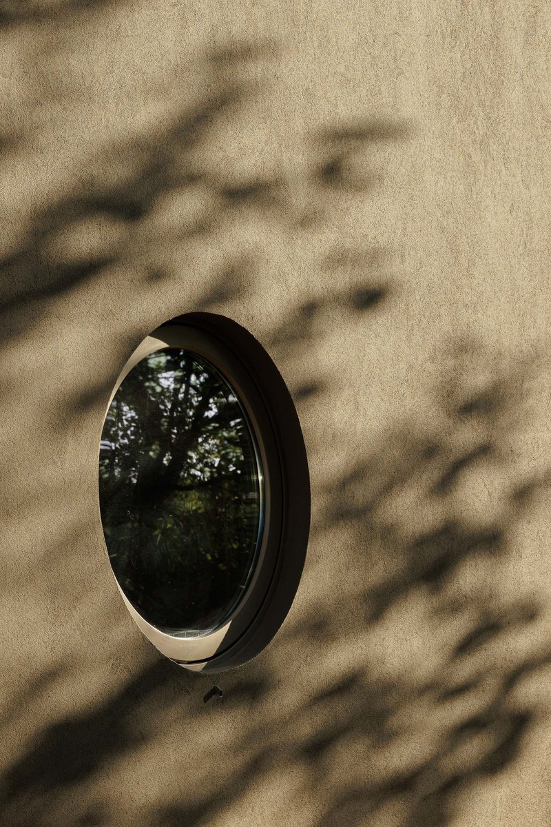 Circular window set in concrete wall with tree shadows cast across the surface