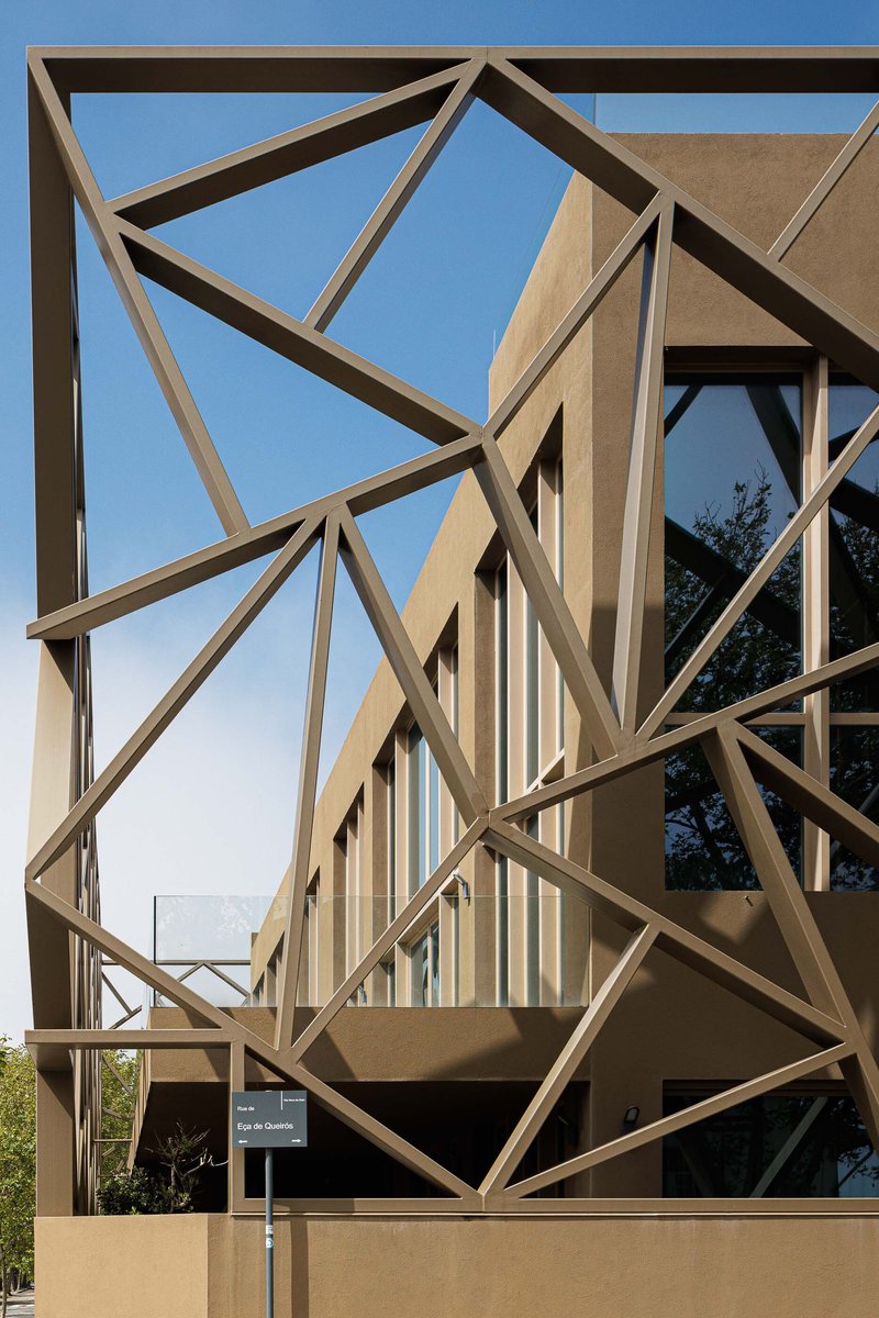 Close-up of the angular steel bracing system wrapping the glazed upper volume in afternoon light