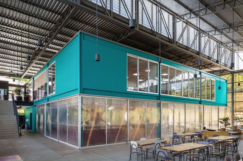 Two-story turquoise volume with translucent lower panels and glazed upper level beneath exposed steel trusses