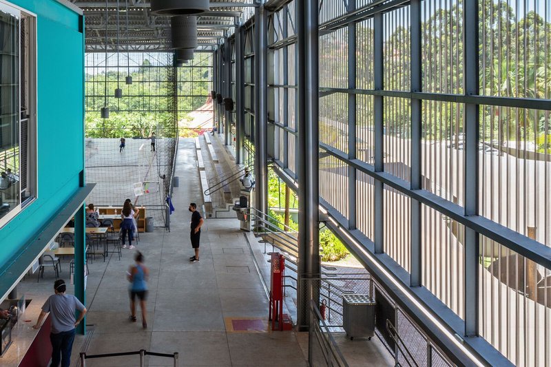 Circulation corridor along corrugated metal facade with people walking beneath exposed structural framework