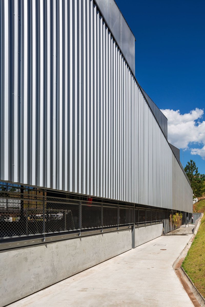 Vertical corrugated metal cladding above chain-link fence and concrete sidewalk under clear blue sky