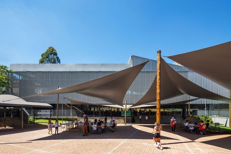 Outdoor courtyard with triangular fabric shade sails on timber poles sheltering visitors at tables