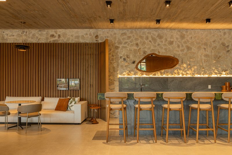 Bar counter with timber stools beneath a river stone wall and board-formed concrete ceiling
