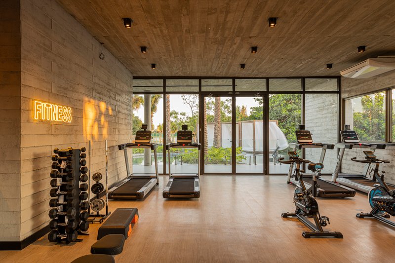 Fitness room with treadmills and equipment beneath board-formed concrete ceiling overlooking vegetation through glazed walls