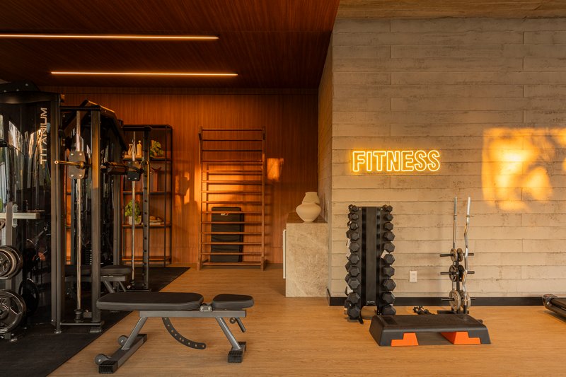 Corner of fitness room with illuminated neon signage and weight racks against concrete and timber walls