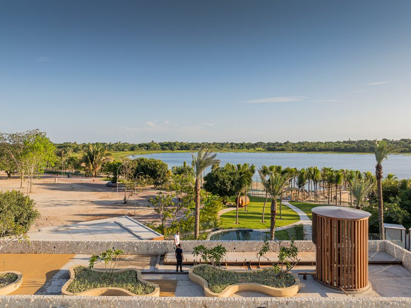 Tiered concrete plaza with planted islands and cylindrical timber tower overlooking a distant lake