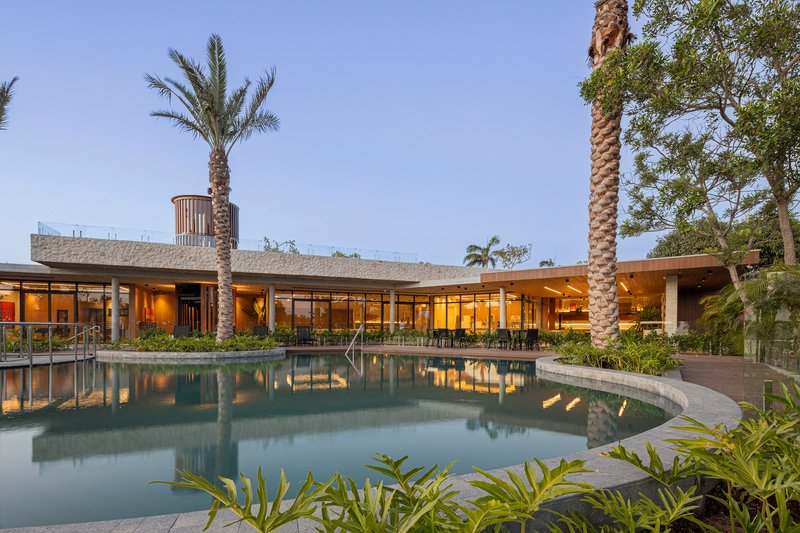Curved pool reflecting the low-slung glazed facade framed by palm trees at twilight