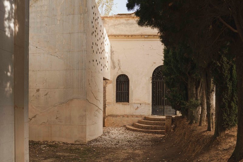 Perforated concrete tower beside stone steps leading to arched doorways framed by tall trees