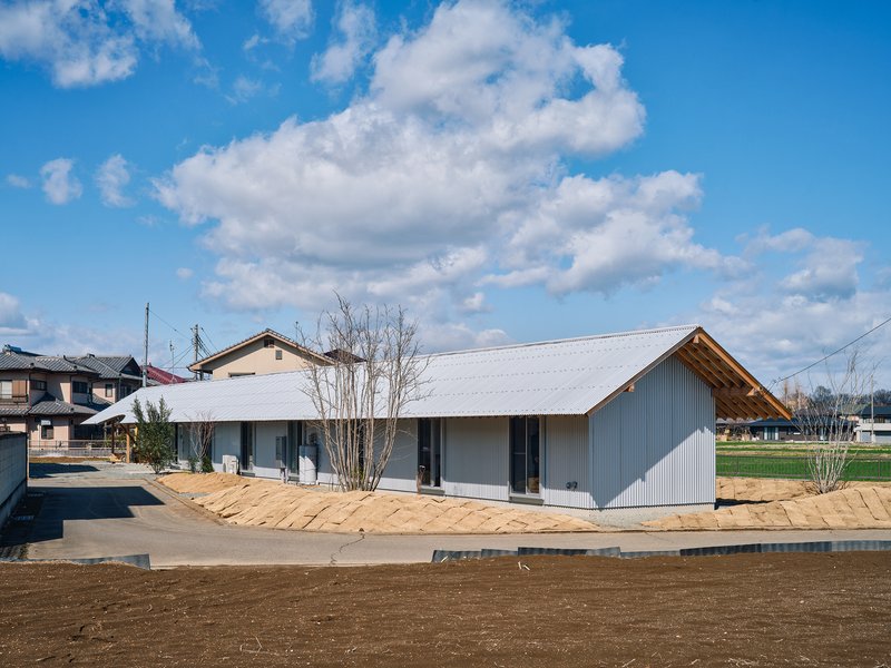 Street view of the corrugated metal volume with gabled roof and timber eaves in a neighborhood setting