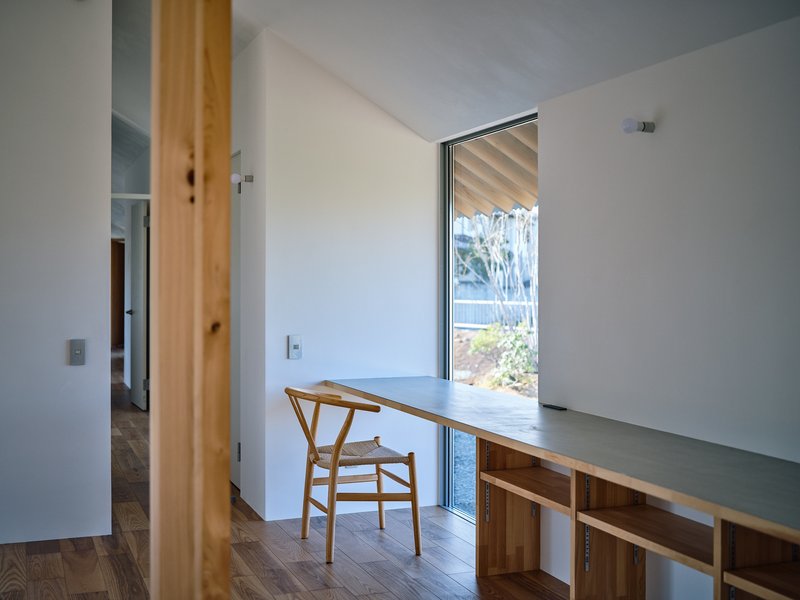 Built-in desk with timber shelving below a tall window framing views of shrubs and trees