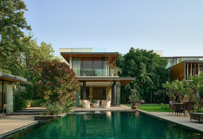 Two-storey glass and timber residence with pool terrace framed by mature trees under afternoon light