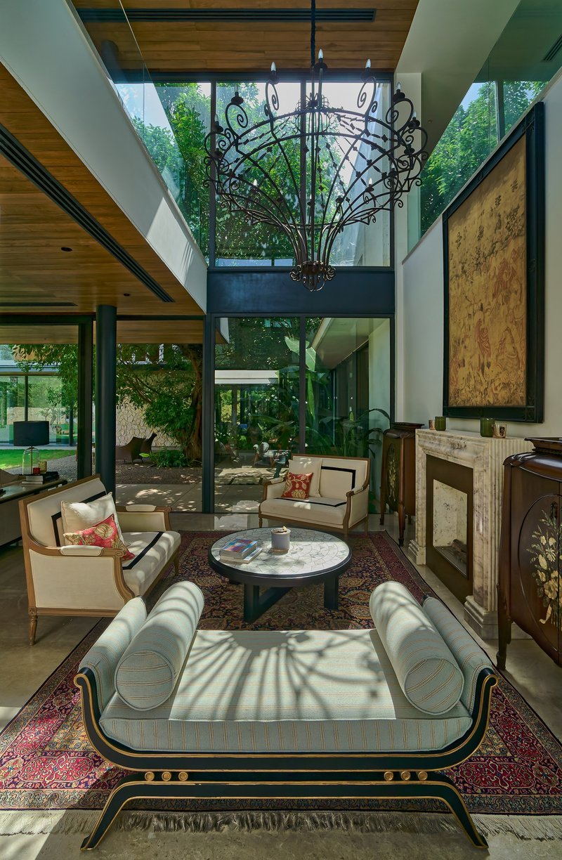 Double-height living room with ornamental metal chandelier suspended above seating and glass walls overlooking garden