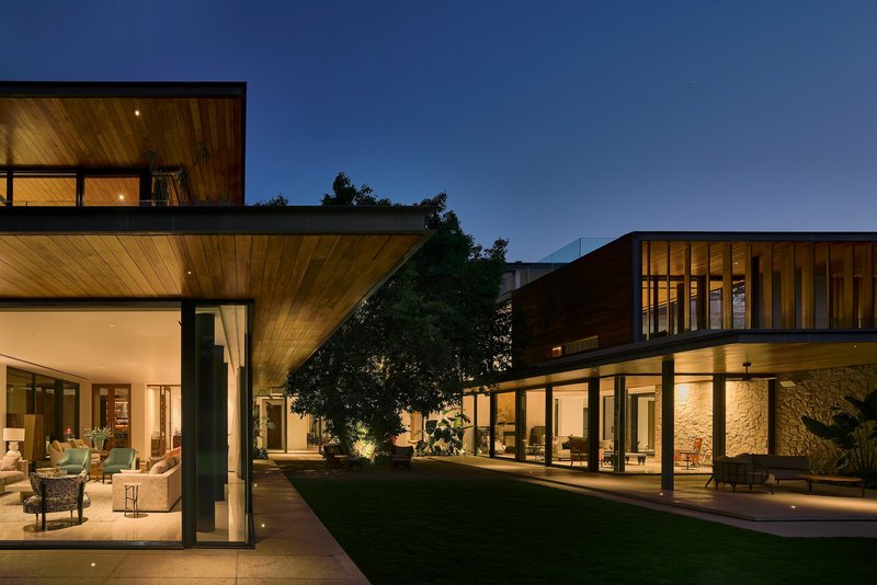 Courtyard view at twilight showing two wings with timber ceilings and lit stone wall between
