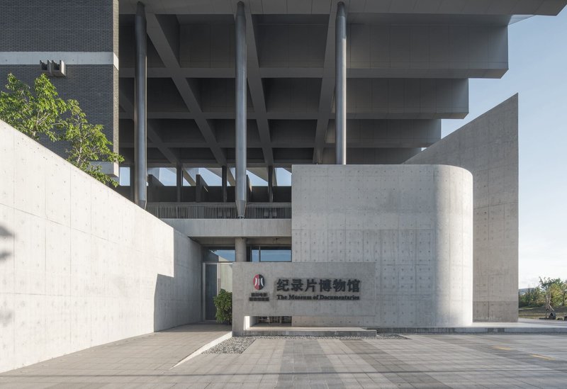 Entrance plaza with cylindrical concrete volume and exposed waffle slab structure above under clear skies