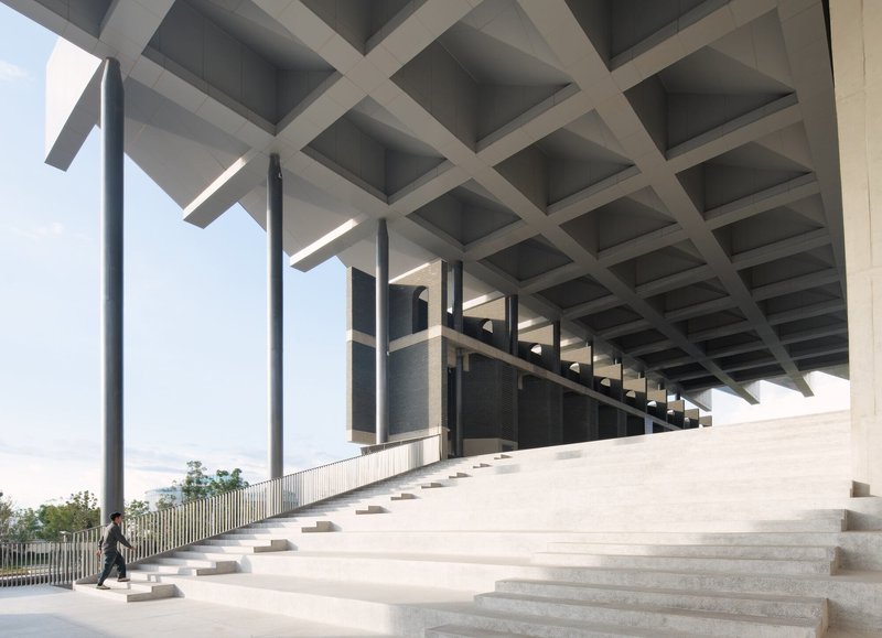 Wide ceremonial staircase beneath a coffered concrete ceiling with a lone figure walking at the base