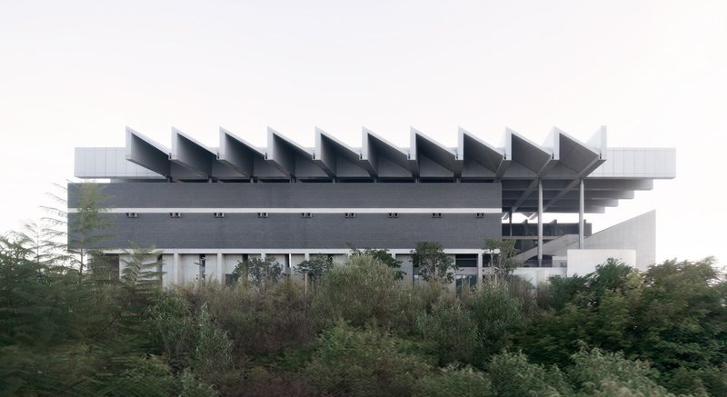 Lateral view of the elevated structure with sawtooth roof profile rising above dense surrounding vegetation