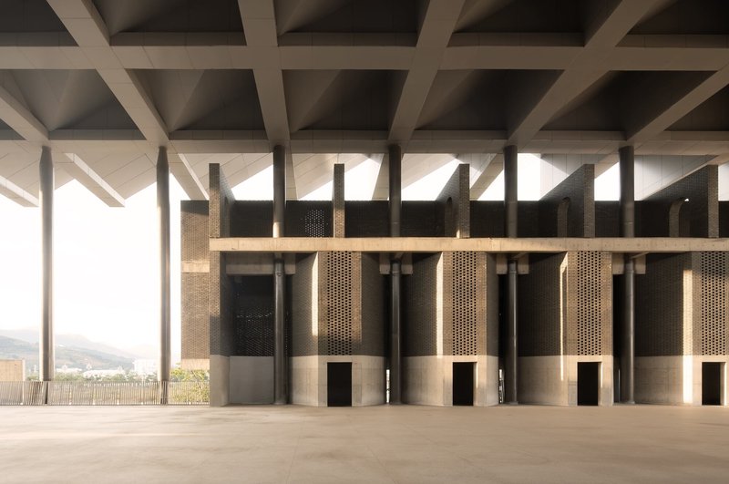 Interior row of perforated bronze cylindrical columns beneath a coffered concrete ceiling