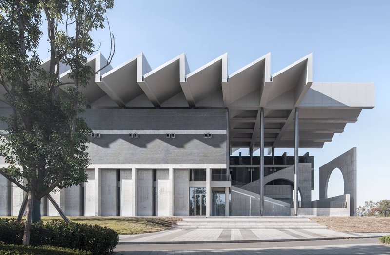 Front elevation showing folded concrete roof forms and arched openings framed by mature trees