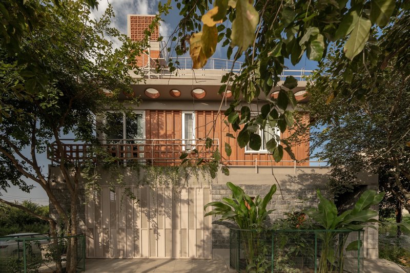Facade with vertical ribbed metal screen at ground level and timber lattice balcony above framed by tropical foliage