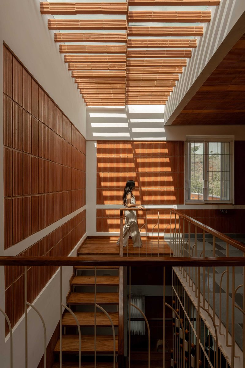 Stairwell with horizontal timber slat skylight casting striped shadows on the wall where a person stands
