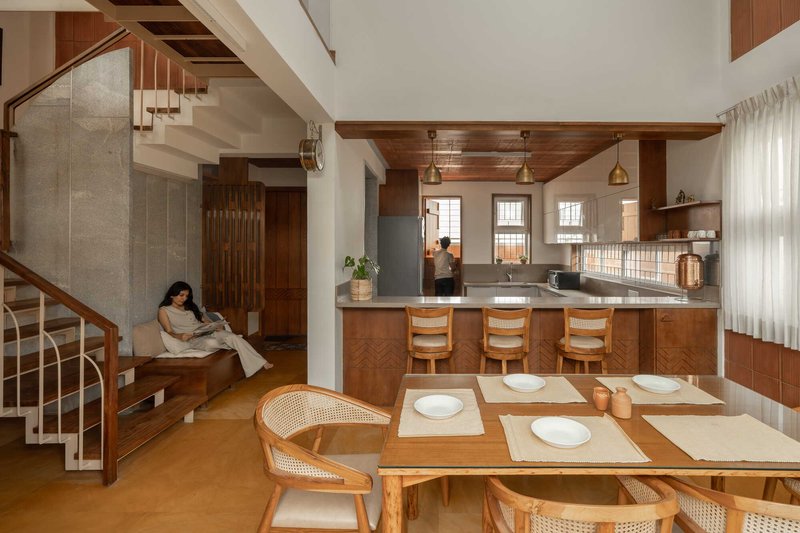 Open plan living space with terracotta tile walls, timber dining table and staircase rising through a double-height volume