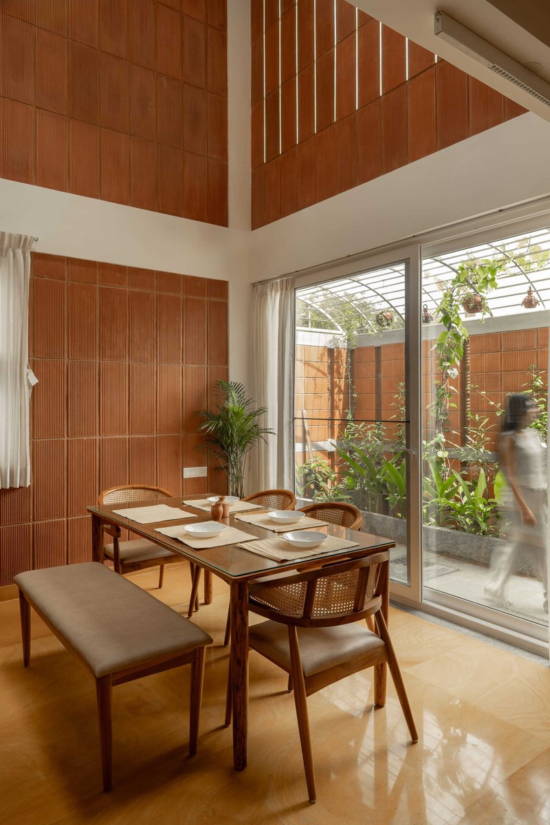 Dining table beside floor-to-ceiling glass doors with a person moving through the adjacent planted courtyard