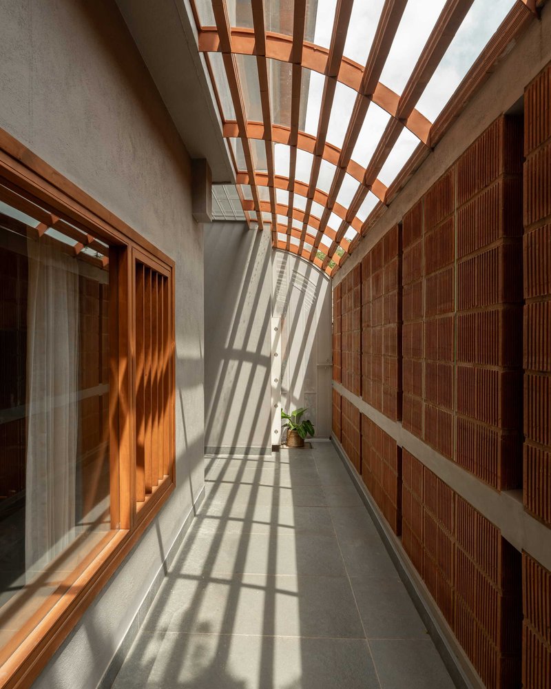 Narrow corridor with timber trellis overhead casting striped shadows across the concrete floor