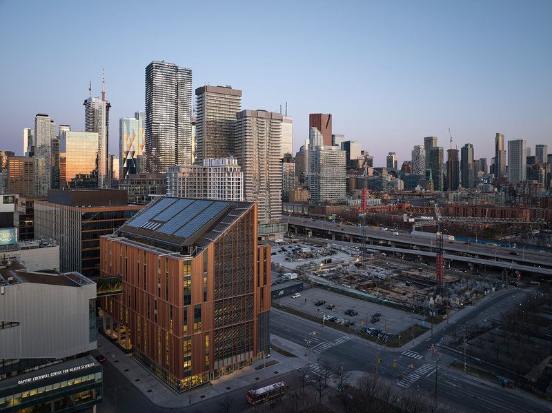 Rooftop view showing the angled solar panel array atop the copper-wrapped volume against the city skyline